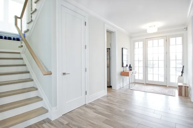 Bright modern home entryway with wooden stairs, white walls, glass French doors, and light hardwood floors.