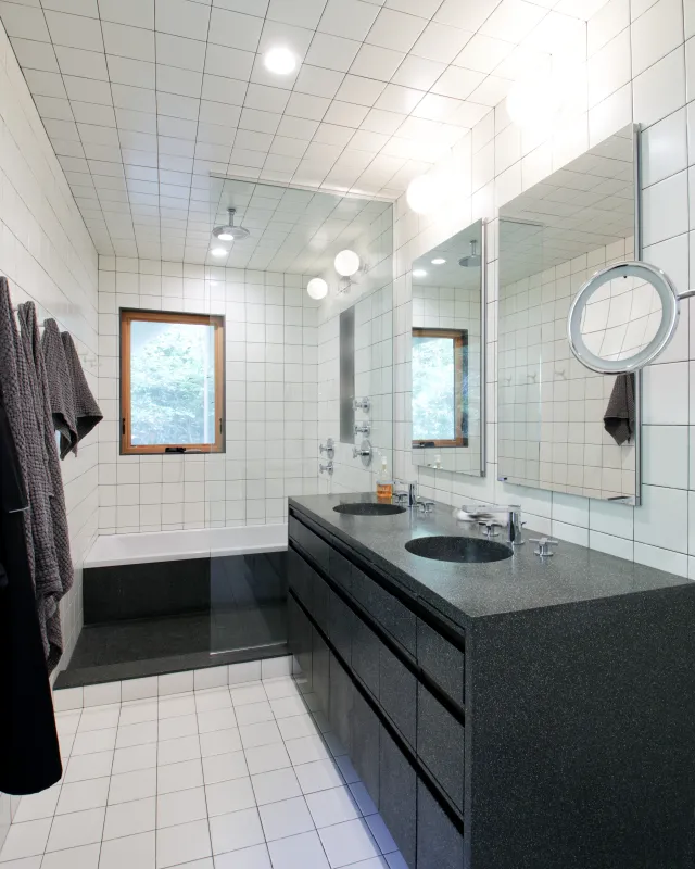 Modern bathroom with white tiled walls, double sink with black granite countertop, and a glass shower enclosure.