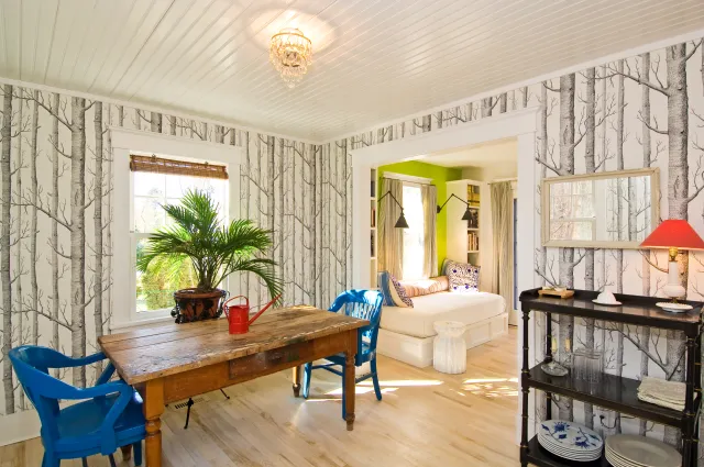 Bright dining room with wooden table, blue chairs, tree-patterned wallpaper, and adjacent green reading nook.