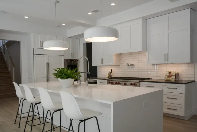 Modern white kitchen with large island, pendant lights, bar stools, and stainless steel appliances