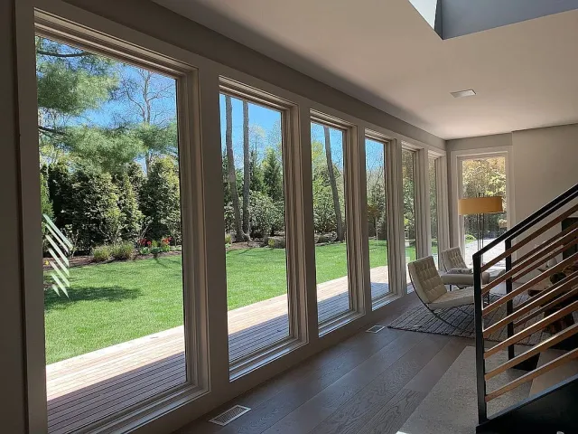 Bright modern room with large floor-to-ceiling windows overlooking a green garden and wooden deck.