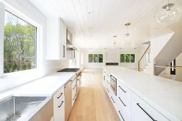 Bright modern kitchen with white cabinets, large island, stainless steel appliances, and natural wood floor.