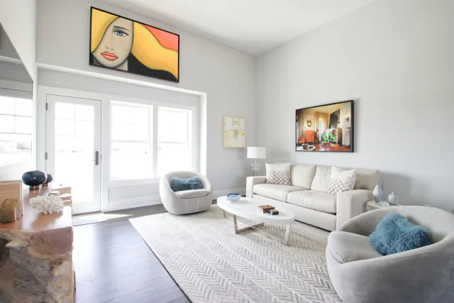 Bright modern living room with beige sofa, round chairs, abstract art, and large windows letting in natural light