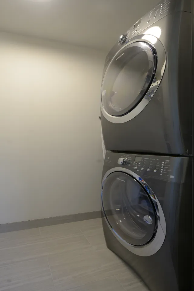 Stacked front-loading washer and dryer in a modern laundry room with light tiled floor and plain walls