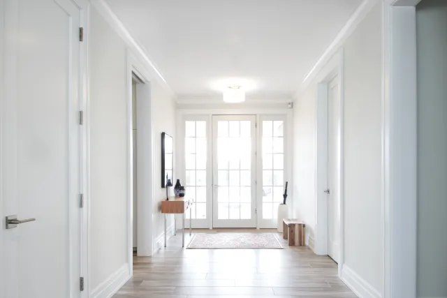 Bright modern hallway with wood flooring, white walls, glass door, console table, and decorative accents.