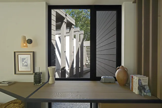 Modern wooden desk by large window showing outdoor architectural elements and decorative items on surface