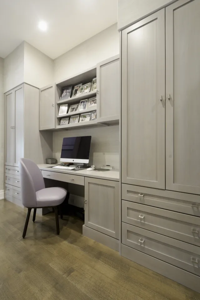 Modern home office with gray cabinetry, computer desk, purple chair, and photo frames on shelves above.