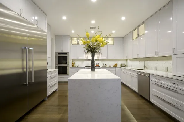 Modern kitchen with white cabinetry, stainless steel appliances, marble island, and yellow floral centerpiece.