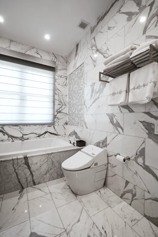 Modern bathroom with marble tiles, a bathtub, a sleek white toilet, and towels on a metal rack.
