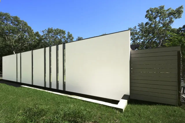Modern minimalist building with white panels and vertical glass strips surrounded by green grass and trees.