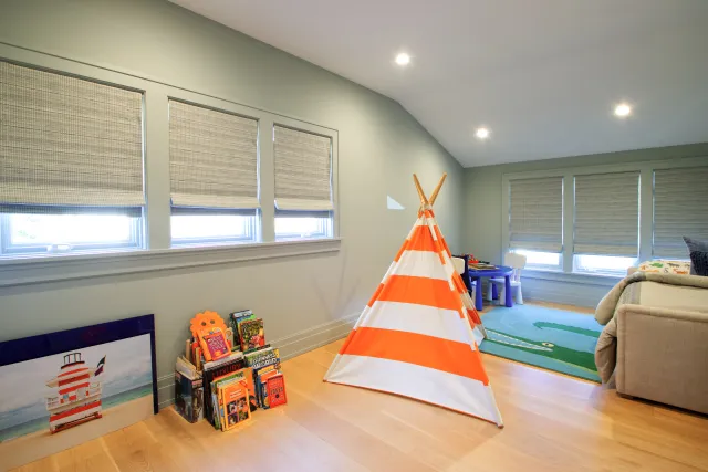 Bright children's playroom with orange striped teepee, books, toys, and window blinds in a cozy space.