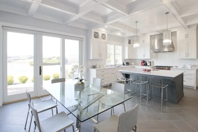 Bright modern kitchen with white cabinets, gray island, glass dining table, and large sliding doors to outside.