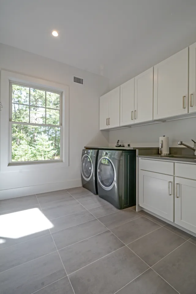 Modern laundry room with black front-load washer and dryer, white cabinetry, and large window with outdoor view.