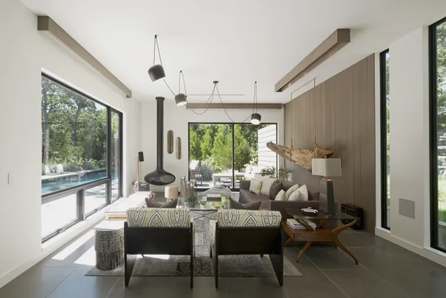 Modern living room with large windows, wood panel wall, suspended fireplace, and cozy seating area with pool view.