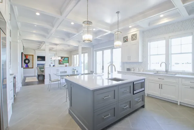 Bright modern kitchen with large gray island, white cabinetry, coffered ceiling, and pendant lights over island.