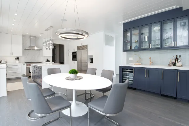 Modern kitchen with white and navy cabinets, stainless steel appliances, round white dining table, and gray chairs