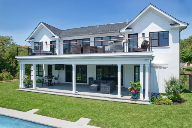 Modern two-story white house with large balcony, patio furniture, and a swimming pool in the backyard.