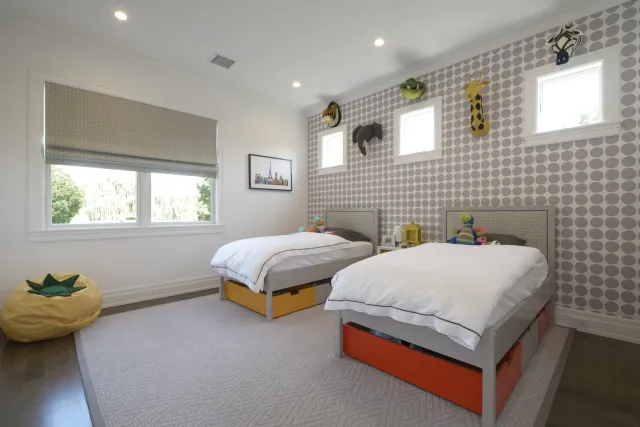 Bright kids bedroom with twin beds, animal wall mounts, geometric wallpaper, and large window with blinds.