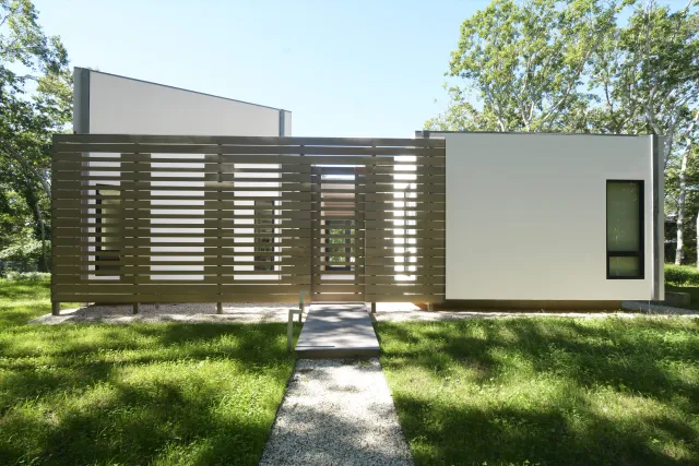 Modern white house with vertical wooden slat screen and narrow windows in a green lawn setting