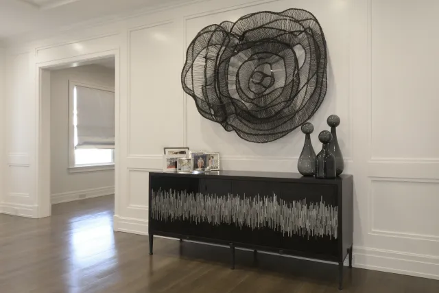 Modern black sideboard with abstract wall sculpture and decorative vases in a bright white room with wood flooring