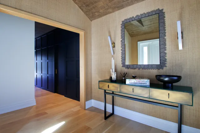 Modern entryway with gold console table, decorative mirror, black bowl, and textured beige walls with black accent wall.
