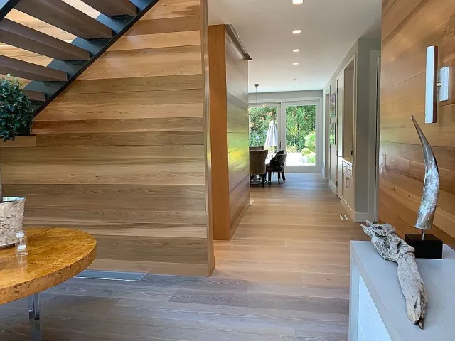 Modern interior with wooden walls and floors, featuring a staircase, dining area, and natural decor elements.