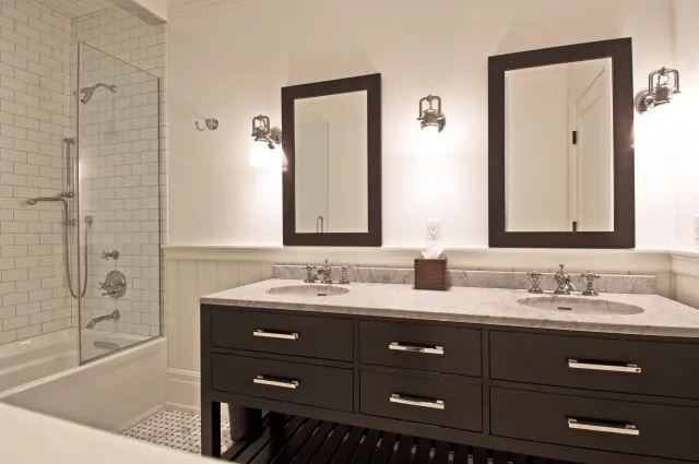 Modern bathroom with double sinks, dark wood vanity, white subway tile shower, and two framed mirrors.