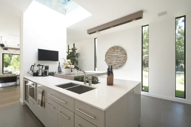 Modern kitchen with white countertops, gray cabinets, skylight, and tall narrow windows overlooking greenery