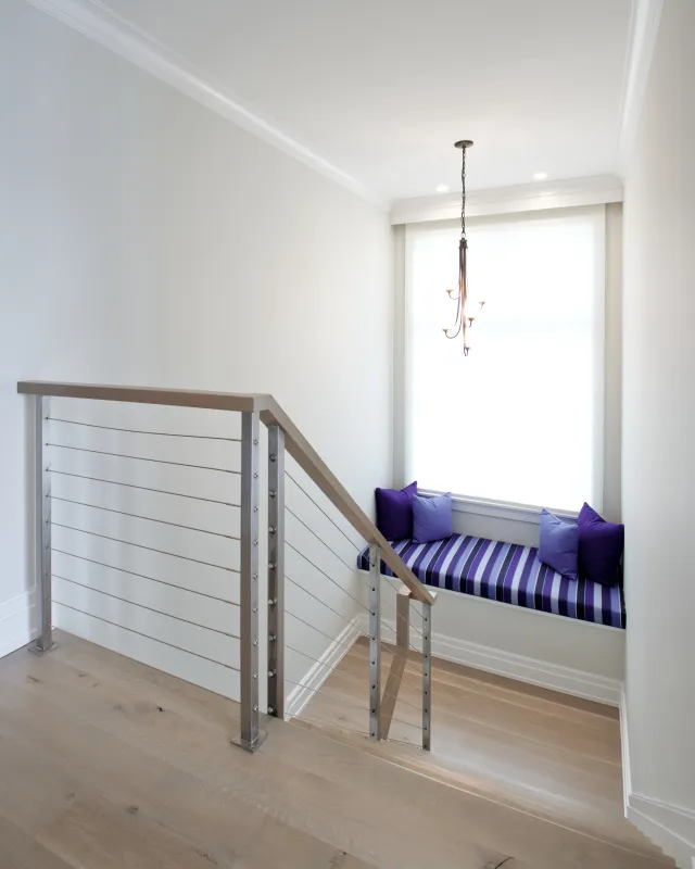 Bright stair landing with modern metal railing and cozy striped window seat with purple cushions.