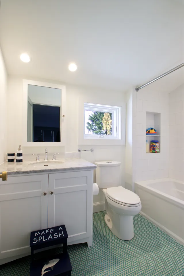 White bathroom with marble countertop, toilet, bathtub, blue patterned floor, and a step stool that reads Make a Splash.