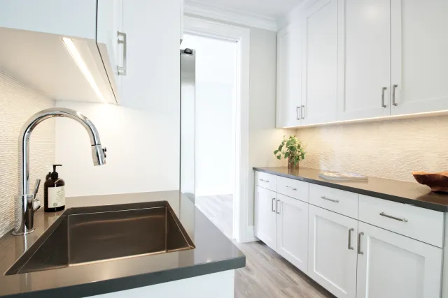 Modern kitchen with white cabinets, black countertops, stainless steel sink, and light wooden floor.