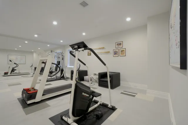 Bright home gym with treadmill, elliptical machine, black leather chairs, wall art, and large mirror