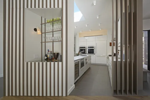 Modern kitchen with white cabinetry, built-in ovens, and a built-in bar with glass shelves and bottles.
