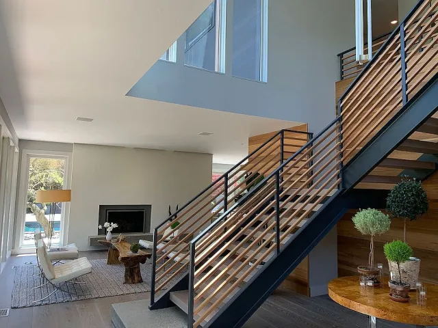 Modern living room with wood and metal staircase, fireplace, natural light, and minimalist furniture.