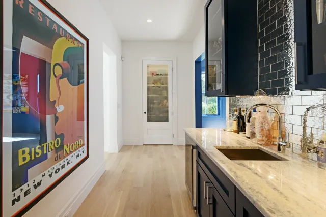 Modern kitchen with navy cabinets, marble countertop, patterned backsplash, and colorful Bistro du Nord poster.