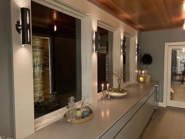 Modern hallway with gray walls, large windows, decorative tray, candles, and long countertop with drawers.