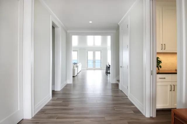 Bright modern hallway with wood flooring leading to living room overlooking ocean through glass doors