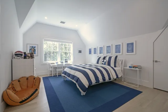 Bright kid's bedroom with striped navy blue bedding, baseball glove chair, and white furniture under slanted ceiling