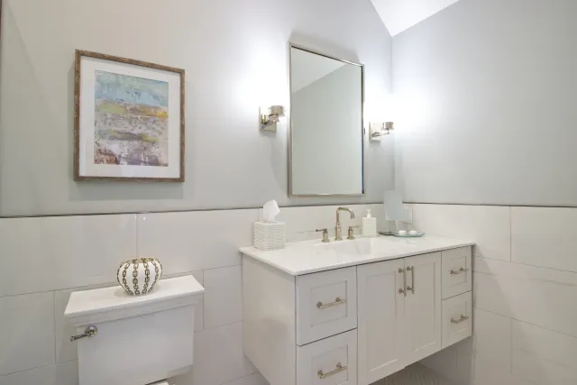 Modern bathroom with white vanity, rectangular mirror, wall sconces, framed artwork, and decorative accessories.