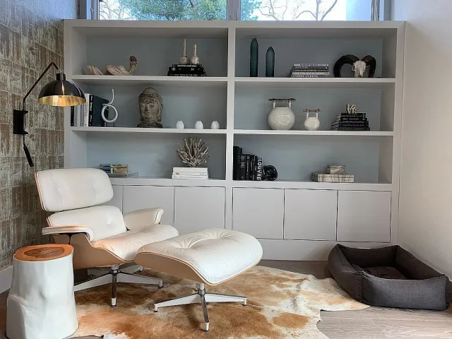 Cozy reading nook with white leather lounge chair, ottoman, modern shelving, and dog bed by window.