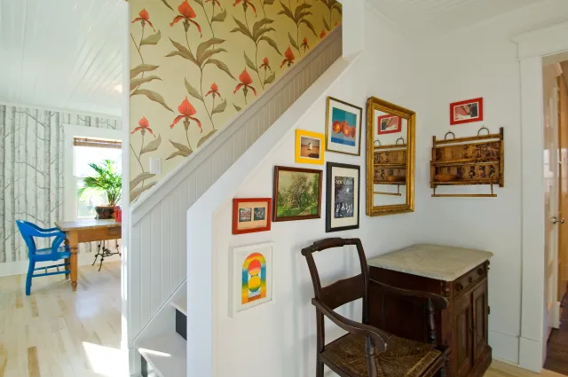 Cozy corner with vintage wooden chair, small desk under stairs, and colorful framed artwork on white walls.