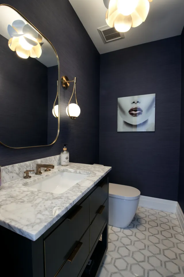 Modern bathroom with dark walls, marble countertop, gold fixtures, geometric floor tiles, and artistic wall print.