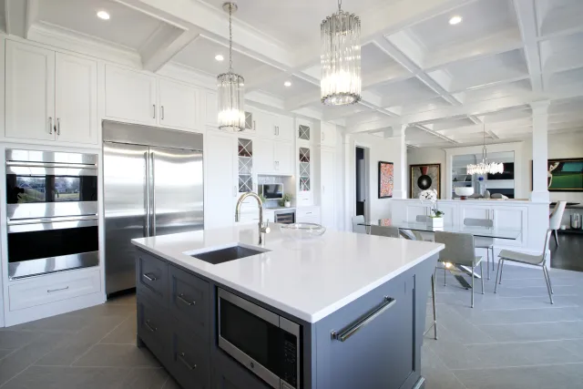 Modern kitchen with white cabinets, stainless steel appliances, large island with sink, and elegant pendant lights