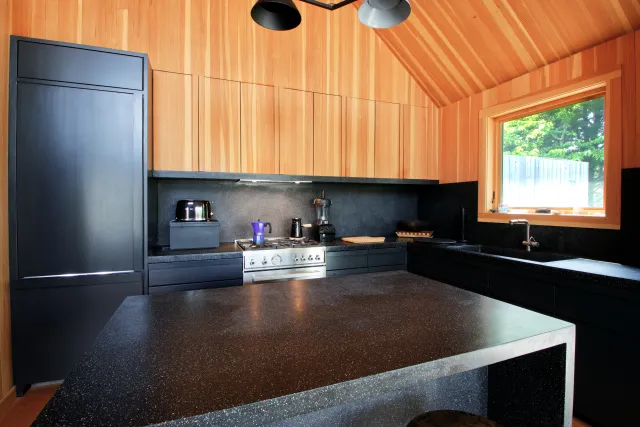 Modern kitchen with black countertops, matte black appliances, light wood cabinets, and natural light from window