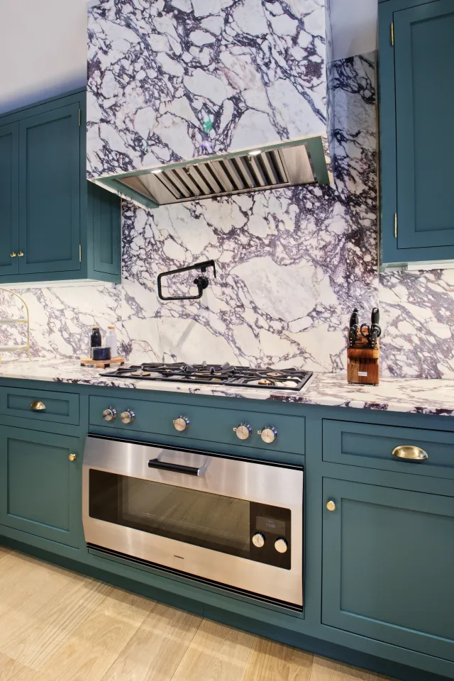 Modern kitchen with teal cabinets, marble backsplash, stainless steel oven, and gas stove with hood vent.