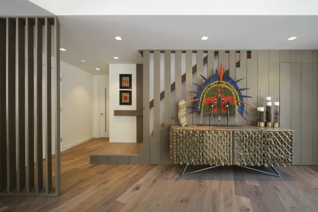 Modern interior with geometric wooden sideboard, colorful tribal mask, and minimalist decor on wood floor.
