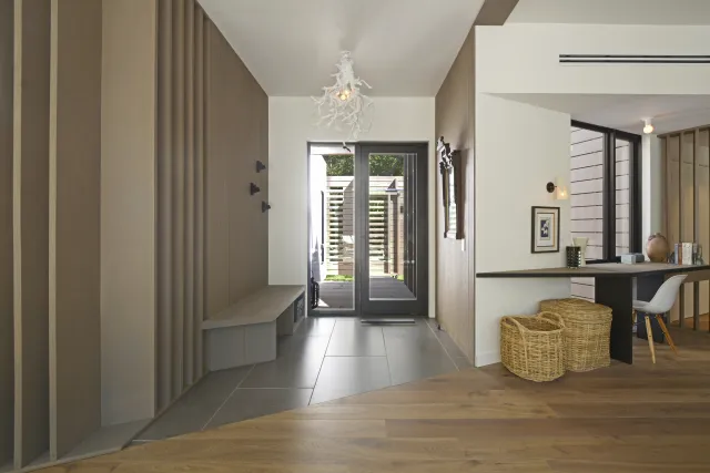 Modern entryway with teak wood paneling, tiled floor, glass doors, white ceiling fixture, and wicker baskets.