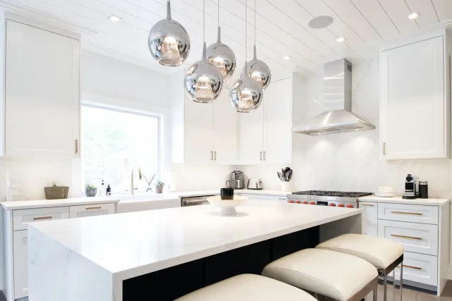 Bright modern kitchen with white cabinetry, marble countertops, large island, and pendant lights