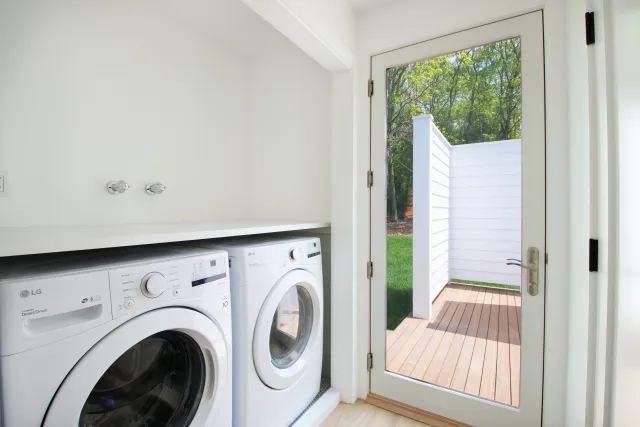 Bright laundry room with white washer and dryer next to glass door leading to outdoor deck.