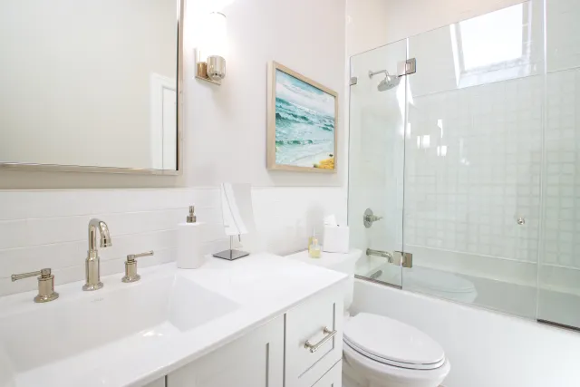 Bright white bathroom with modern sink, glass shower enclosure, and coastal wall art.